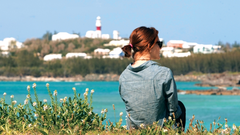 A woman facing away from the camera with the view of Cooper's Island lighthouse in the foreground.