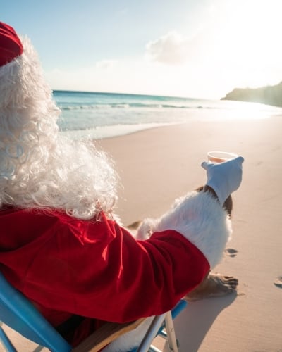 Santa is sitting on the beach with a cocktail.