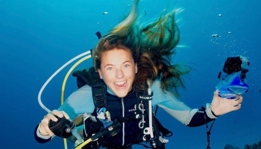 A woman is underwater smiling at the camera.