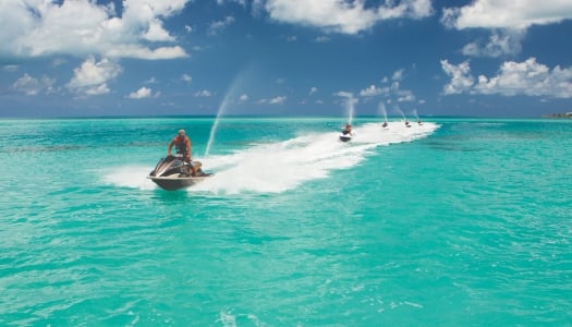 A group of guys are travelling on jetskis.
