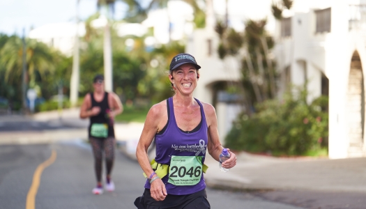 A woman is smiling at the camera while running the PWC Half Marathon.