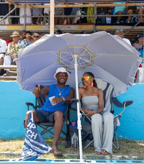 A couple is sitting under a tent court side at Cup Match.