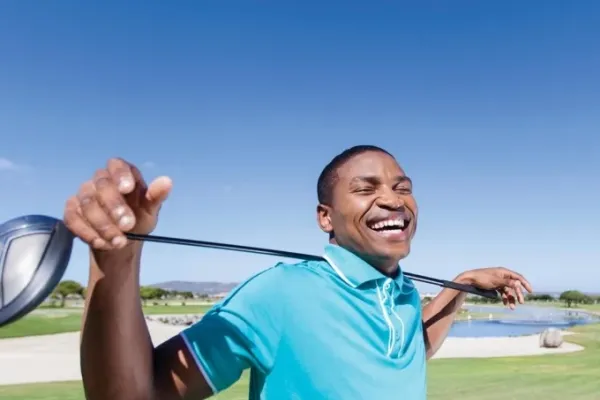 A smiling man resting a golf club on his shoulders at a Bermuda golf course