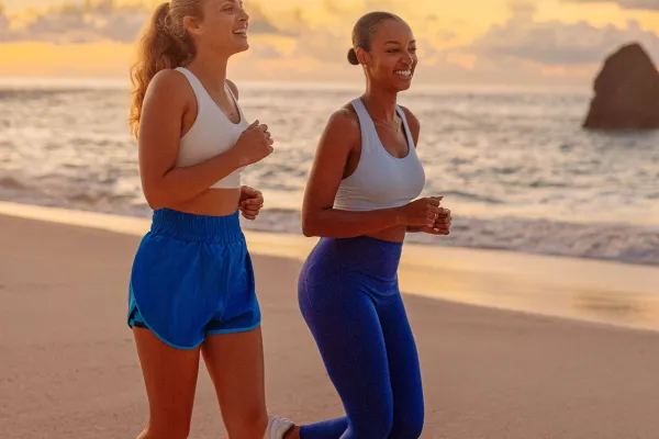 Two girls are running on the beach.