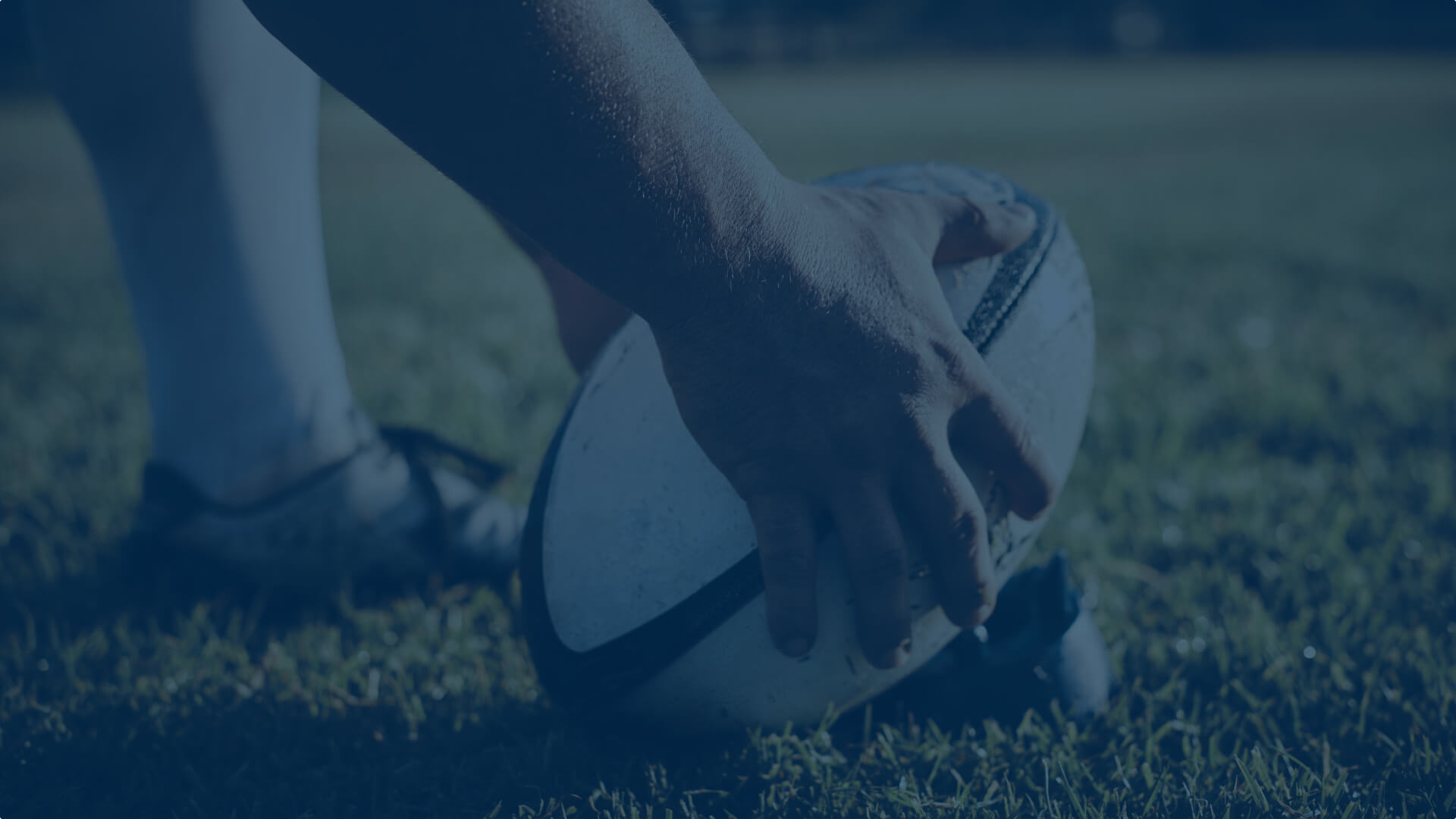 Hands holding a rugby ball on ground