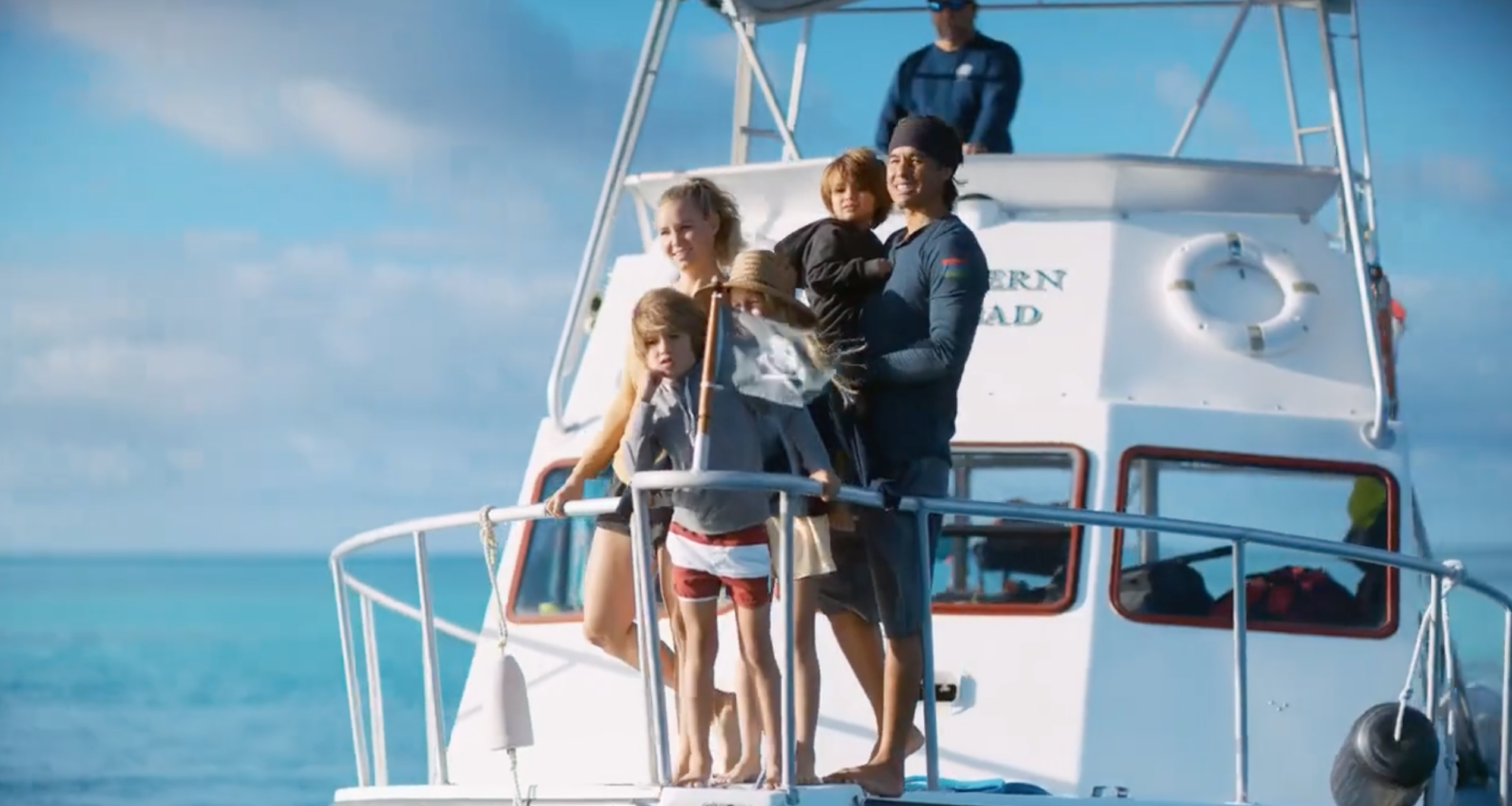 A family is standing on a boat looking out at a sunken vessel.