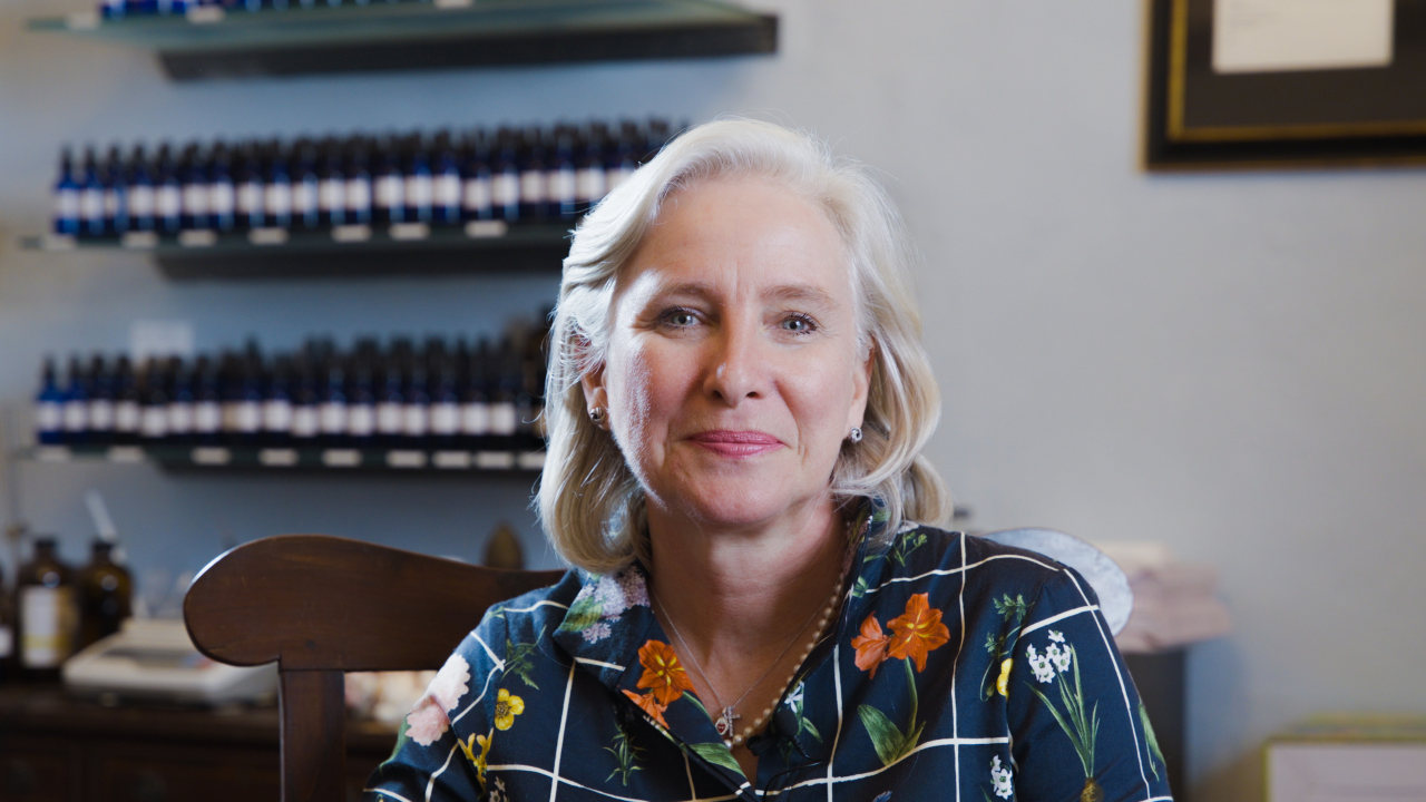 A woman is smiling at the camera with perfume scents behind her.