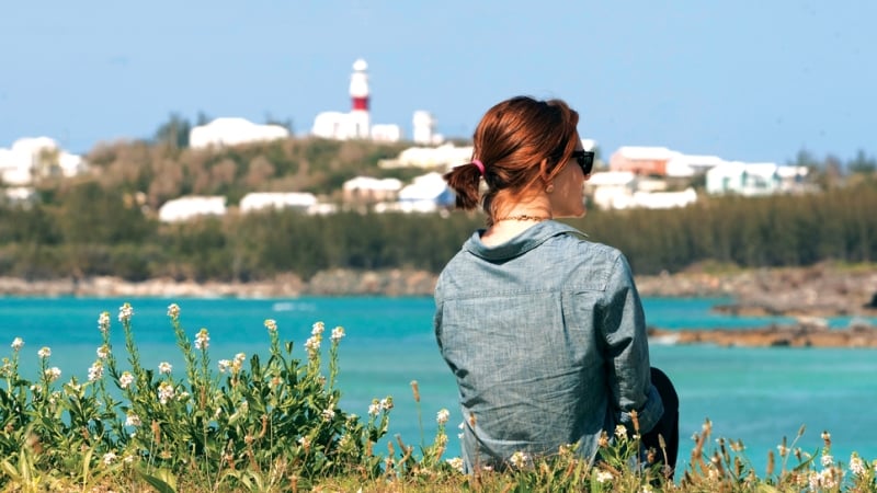 A woman facing away from the camera with the view of Cooper's Island lighthouse in the foreground.