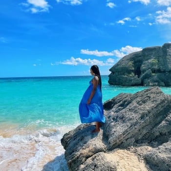 A woman in a blue dress standing on a rock on a beach