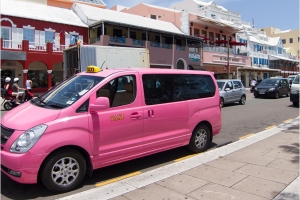 A pink taxi van parked on the side of a road.