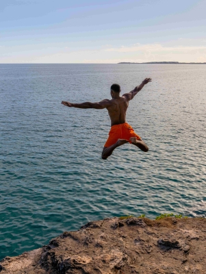 A man is star jumping into the ocean from a cliff.