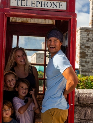 A family is piled up in an old style British telephone booth smiling at something in the distance.