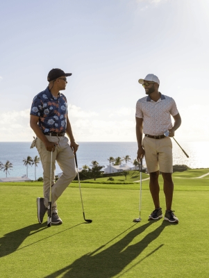 Two men are standing on a golf course talking. 