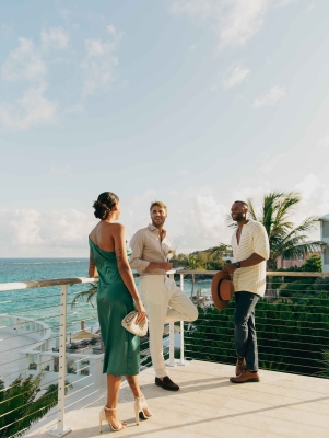 A woman and two men are standing on a balcony laughing. 