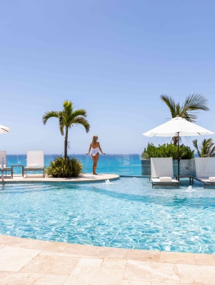 A woman is on a pool deck looking at the ocean. 