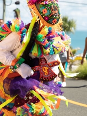 A close up of a gombey dancer with people dancing and walking behind.