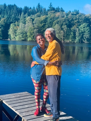 A couple are standing on a dock smiling at the camera.