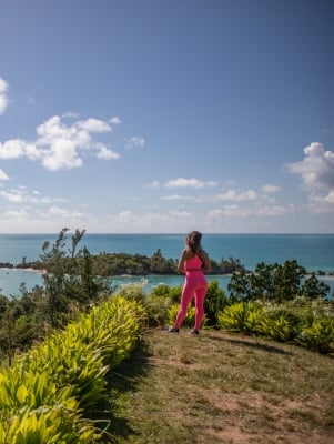 A woman is looking out at the water from a grassy viewpoint.