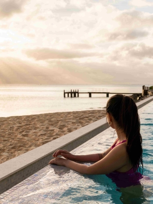 A woman is standing in a pool looking at sunrise.