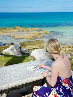 A woman is painting by the sea.