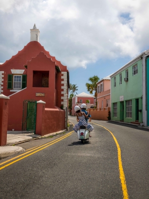 A couple is riding a scooter by colourful buildings.