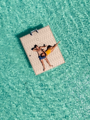 A couple is cuddling while floating on a dock surrounded by turquoise waters.