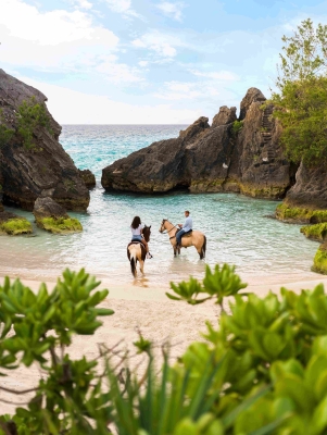 A couple are on horses in a secluded beach.
