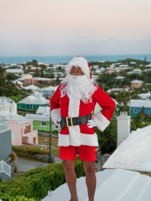 A man dressed as Santa is standing on a Bermuda house roof.