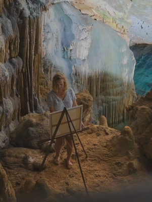 A woman is painting on an easel in a scenic cave grotto.