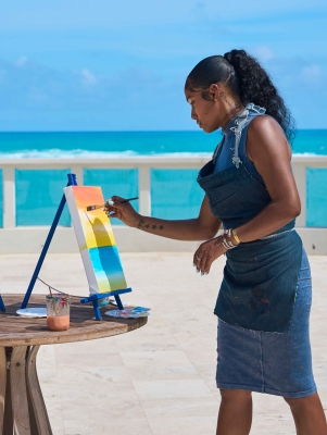 A woman is painting by a scenic background.