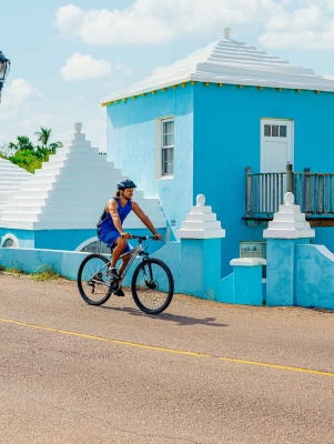 A man is riding a bike next to a blue pastel building.
