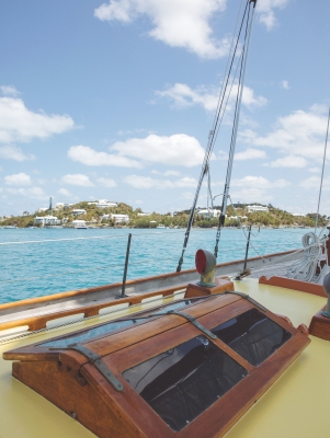 Exterior view of a sail boat with island houses and greenery in the background.