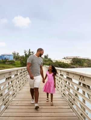 A father and daughter are walking along a bridge smiling.