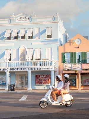 Two people are driving down Front Street on a Scooter