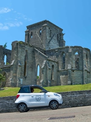 A microcar is driving passed the unfinished church