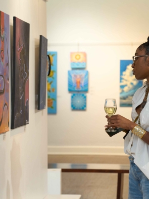 A woman is holding a glass of wine staring at art on a wall
