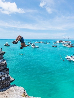 A person doing a backflip off a rock into the sparkling blue waters of Bermuda