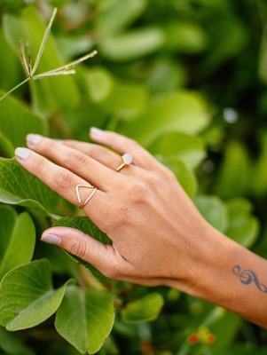 A hand with handmade jewellery is in front of a lush green bush.