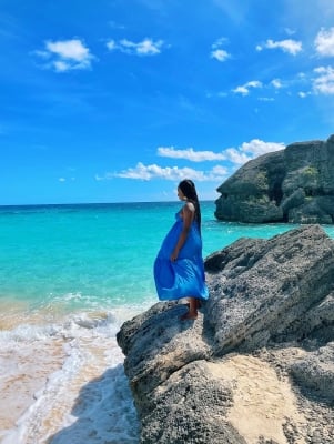 A woman in a blue dress standing on a rock on a beach