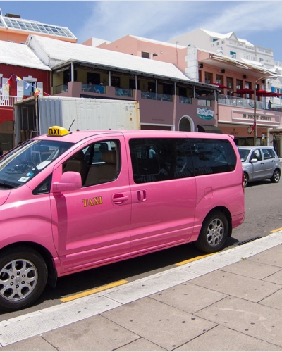 A pink taxi van parked on the side of a road.