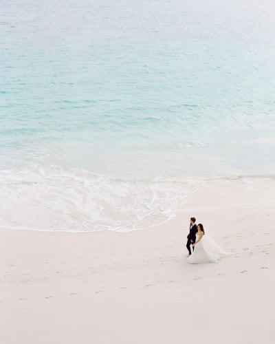 A bride and groom walking on the beach