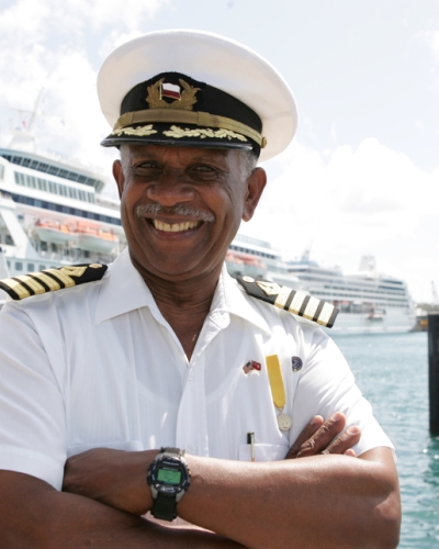 A boat pilot is smiling at the camera with three cruise ships behind him.
