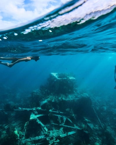 Two people are snorkeling in clear water around a shipwreck.