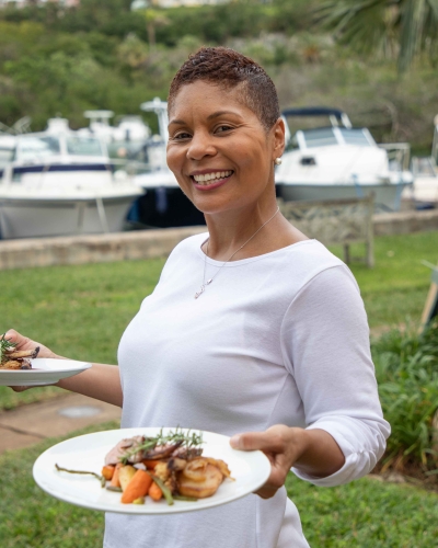 A waitress is smiling at the camera with three plates in her hands.