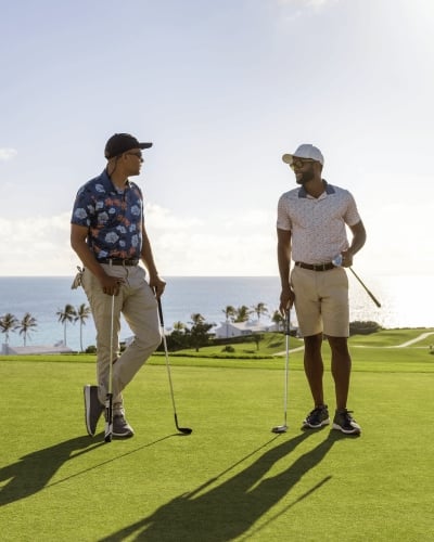 Two men are standing on a golf course talking. 