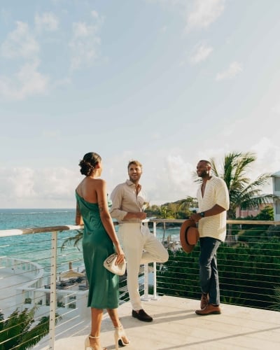 A woman and two men are standing on a balcony laughing. 