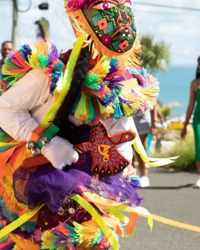 A close up of a gombey dancer with people dancing and walking behind.