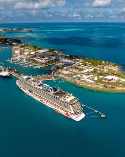 An aerial view of two large cruise ships in calm waters by a port.