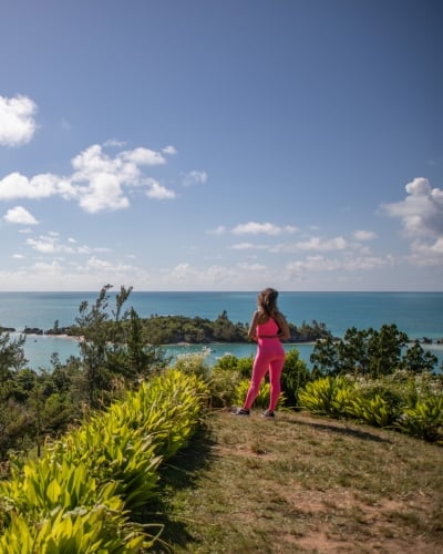 A woman is looking out at the water from a grassy viewpoint.