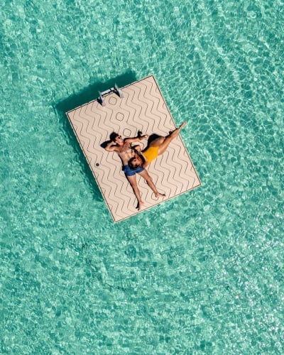 A couple is cuddling while floating on a dock surrounded by turquoise waters.